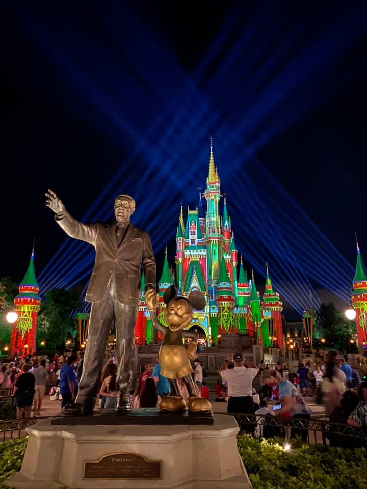 Walt Disney and Mickey Mouse statue with red and green Disney World castle in the background